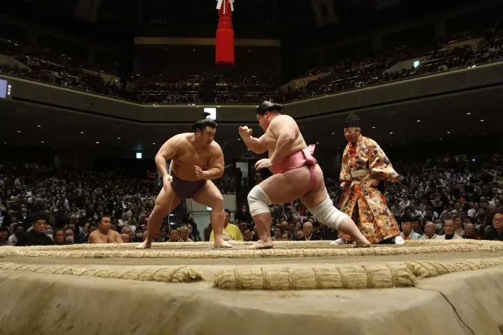 Sumo wrestlers demonstrating shiko leg-stomping at a casual sumo experience in Osaka, Japan