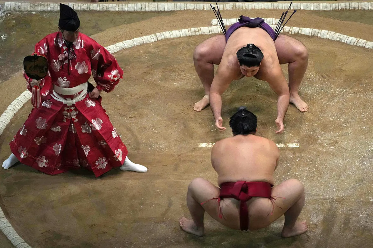 Two sumo wrestlers clashing in a bout at a dedicated sumo hall in Japan — elevated ring with spectators