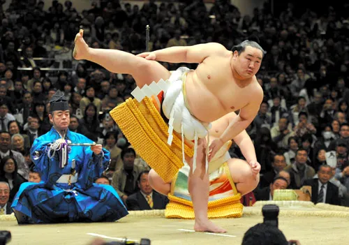 Tourists seated on the floor of an Osaka sumo stable watching professional wrestlers in morning practice (asageiko)