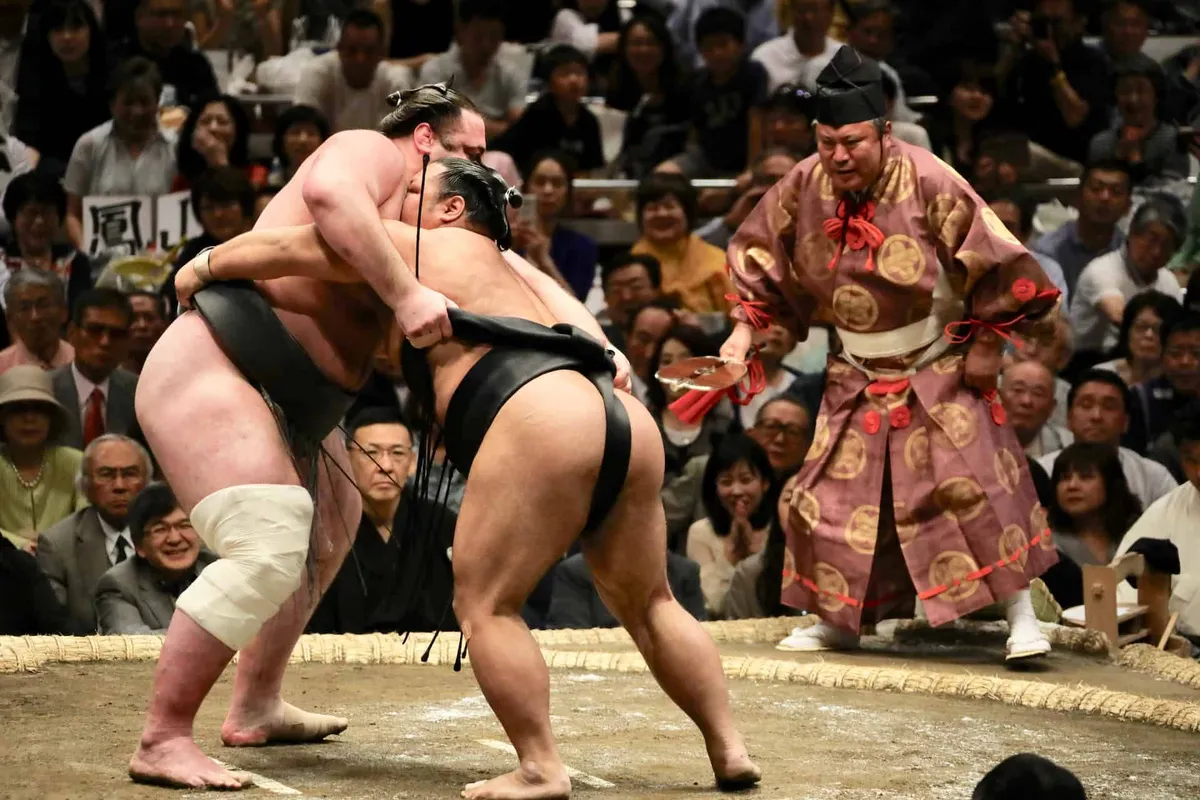 A tourist wearing a traditional mawashi belt stands inside a sumo dohyo ring in Japan